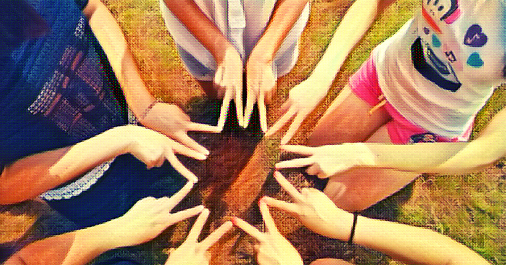 a group of friends sit on their knees and hold their pointer finger and middle finger in a V shape on both hands, then all touch their finger tips together forming a star or flower shape.