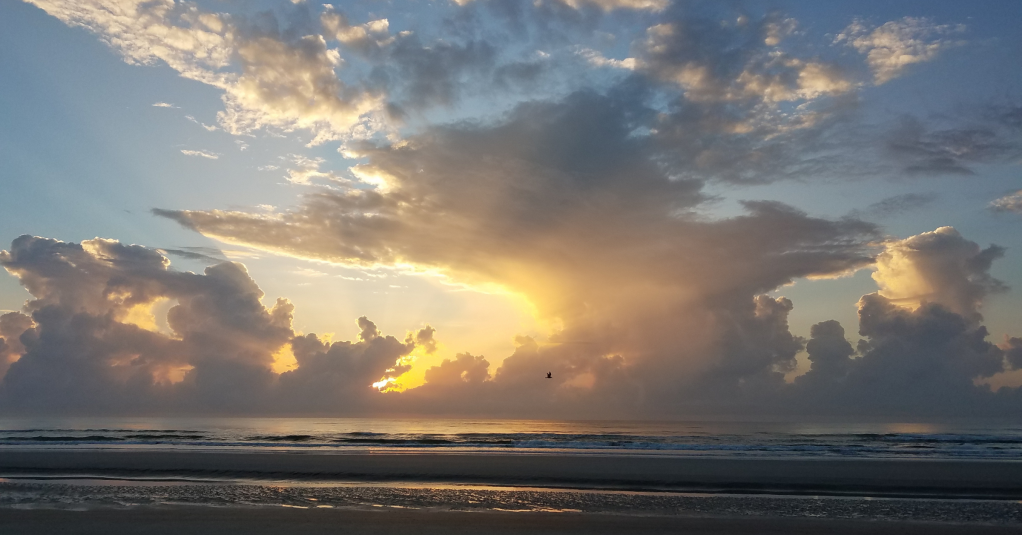 A beautiful sunrise on St. Augustine beach. Clouds add dimensions of colors with golden beams of light bursting through and reflecting off the Atlantic Ocean.